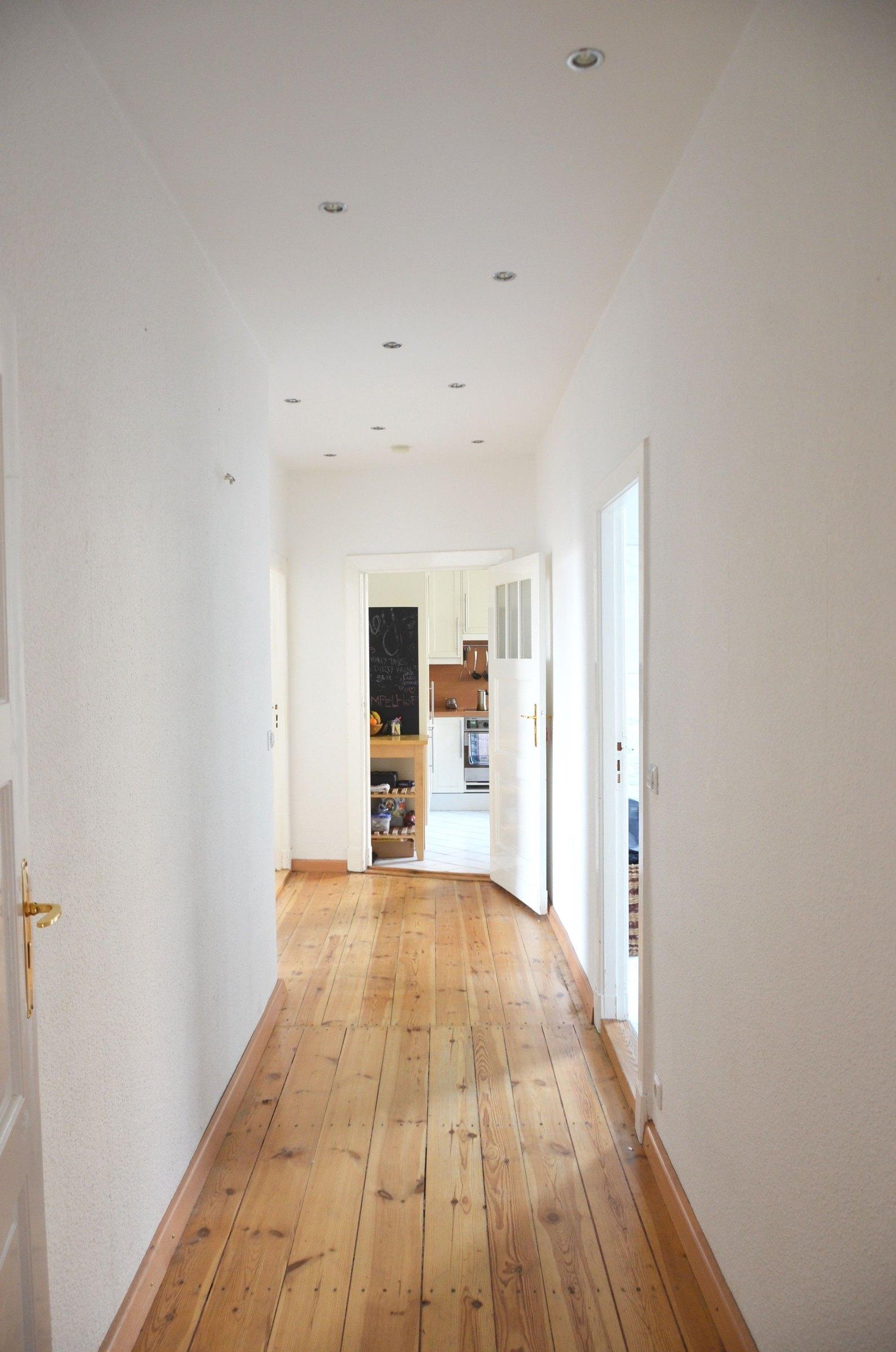 Renovierter Wohnungsflur mit aufgearbeitetem Dielenboden, weißen Wänden und neuer Deckenbeleuchtung
